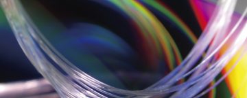 Bundle of clear glass fibers up close, multicolored backdrop
