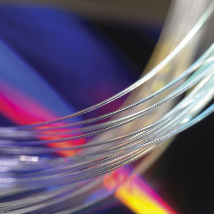Bundle of clear glass fibers up close, multicolored-lighted backdrop