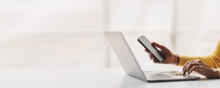 Hands holding a smartphone in front of a laptop