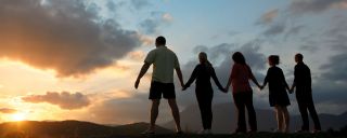 People hold hands for balance on hill facing sunset