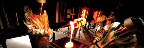 Workers in protective suits pour molten glass from crucible