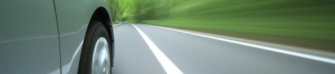 Right-side, tire-level view of gray car traveling road