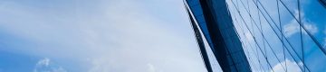 Tall building covered in glass windows that reflect blue sky