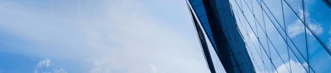 Tall building covered in glass windows that reflect blue sky