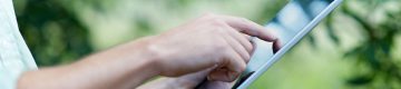 Person touches electronic notebook with forefinger, trees in background