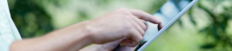 Person touches right forefinger to electronic device, trees in background