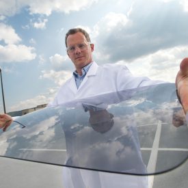 Man in white lab coat holds curved glass windshield