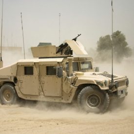 Humvee cor de areia levanta poeira conforme percorre a estrada