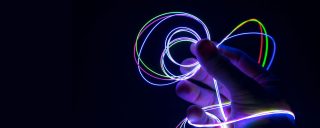 Pessoa segura uma fibra difusora de luz colorida, brilhando no escuro