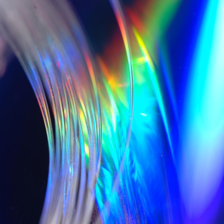 Closeup of bundle of clear glass fiber, multicolored-lighted backdrop
