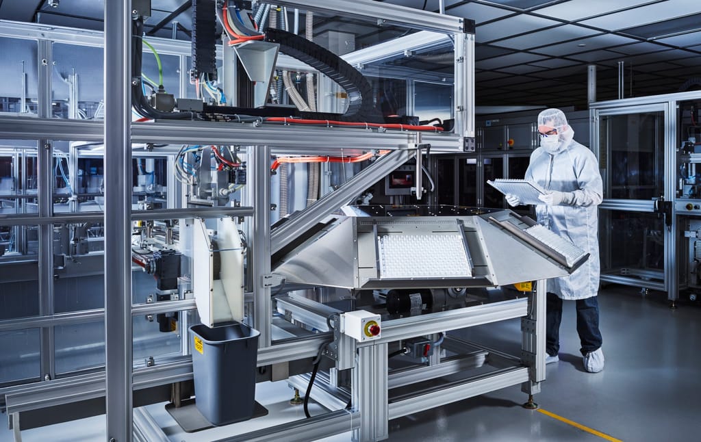 A Corning technician in cleanroom whites inspecting a pharmaceutical vial production line