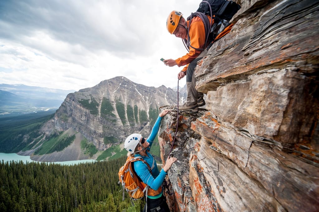 Two rock climbers on a cliff face, one reaching up to the other