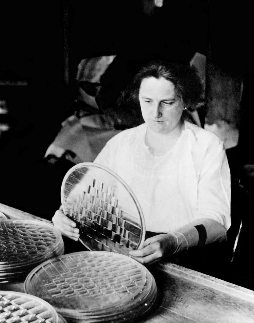 A 1920s Corning glass inspector examining a perforated disc