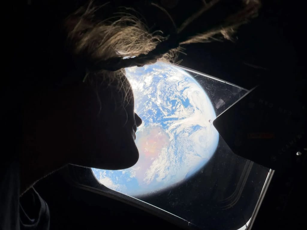 Artemis II astronaut Christina Koch silhouetted at a spacecraft window, looking out at Earth