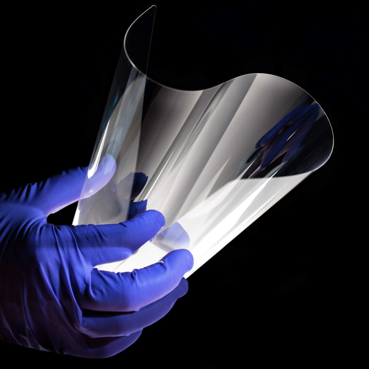 Disembodied hand in purple latex gloves bending Corning glass in stylized moody shot on dark background