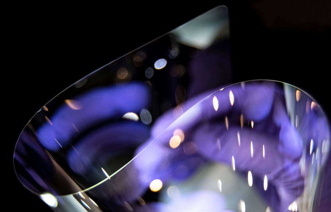 Disembodied hand in purple latex gloves bending Corning glass in stylized moody shot on dark background