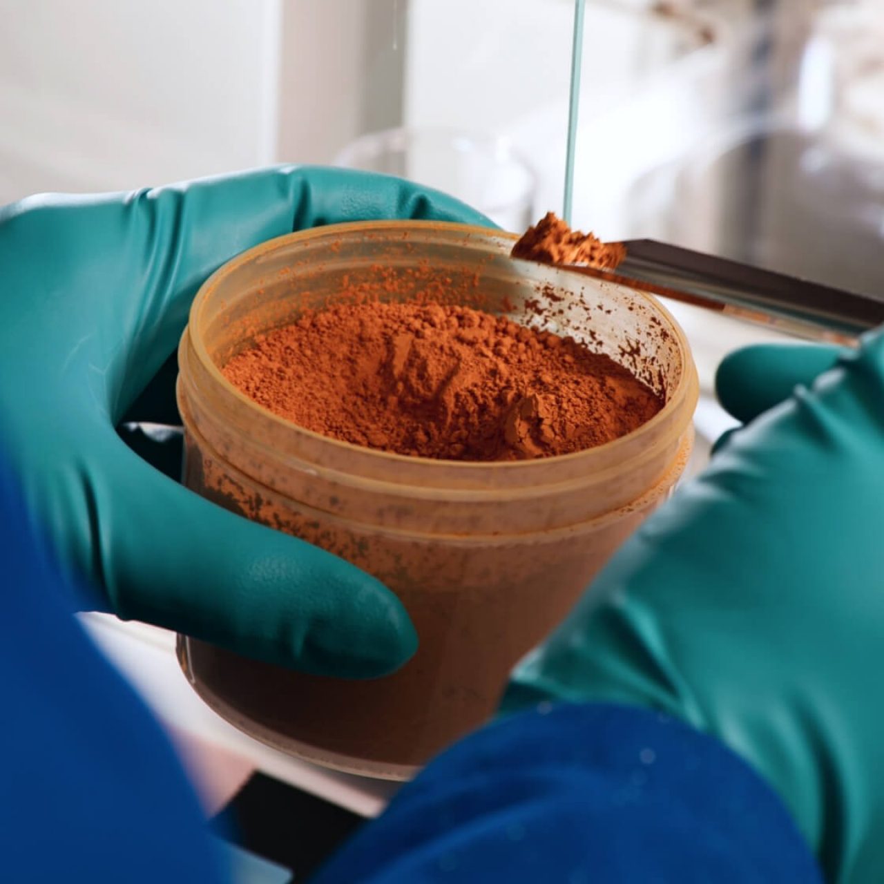 A copper colored powder is carefully spooned out of a container.