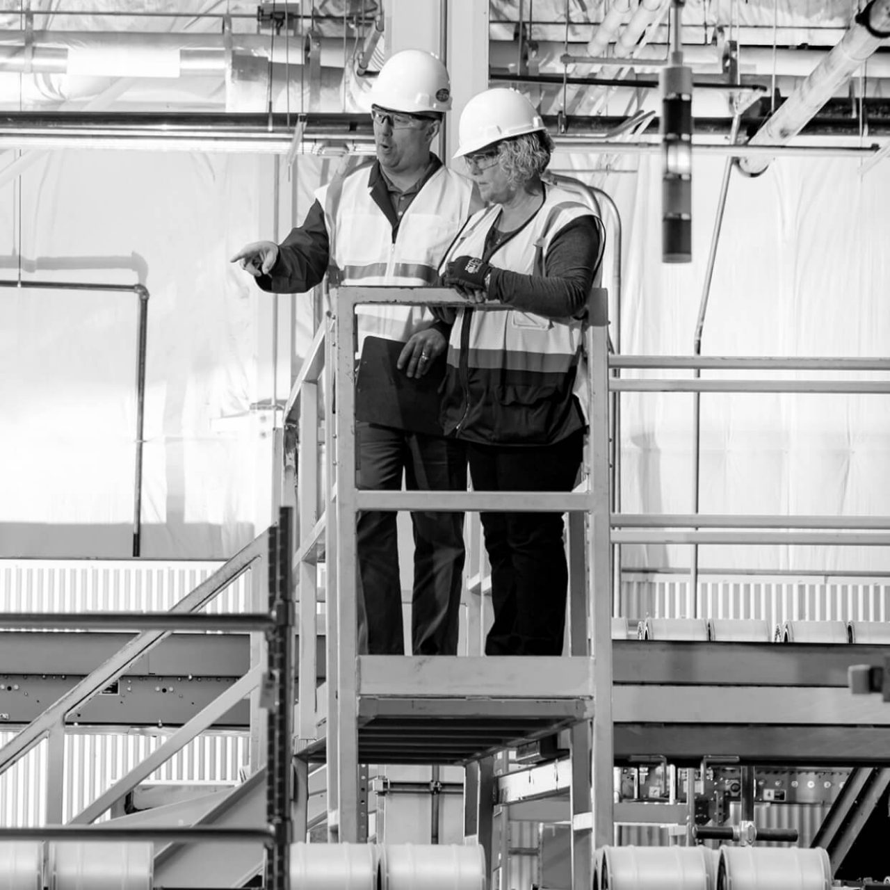 Industrial setting with two people in hard hats at the top of a metal stairway.