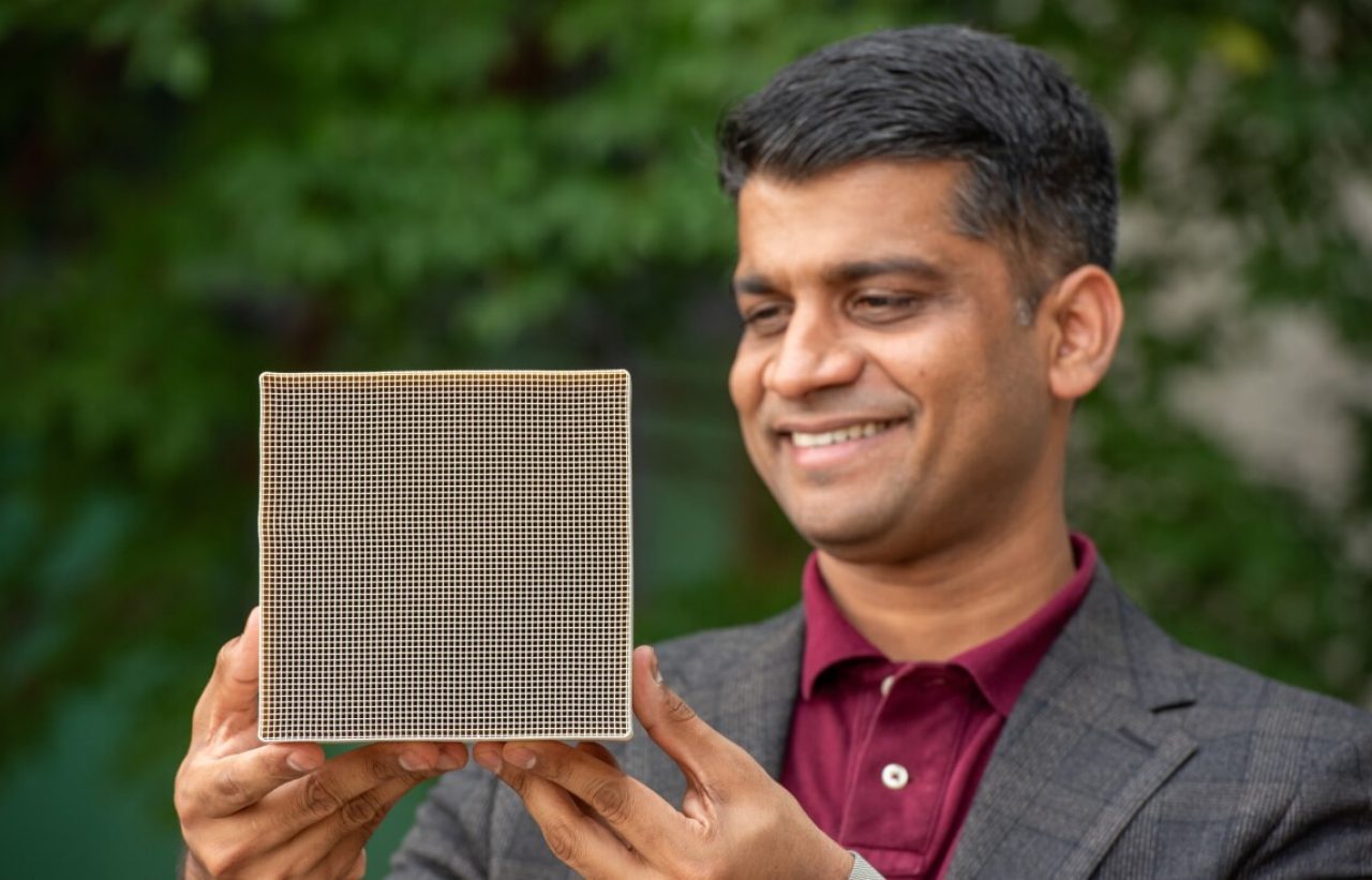 Jayant Rane wearing a jacket and red shirt holds a honeycomb.