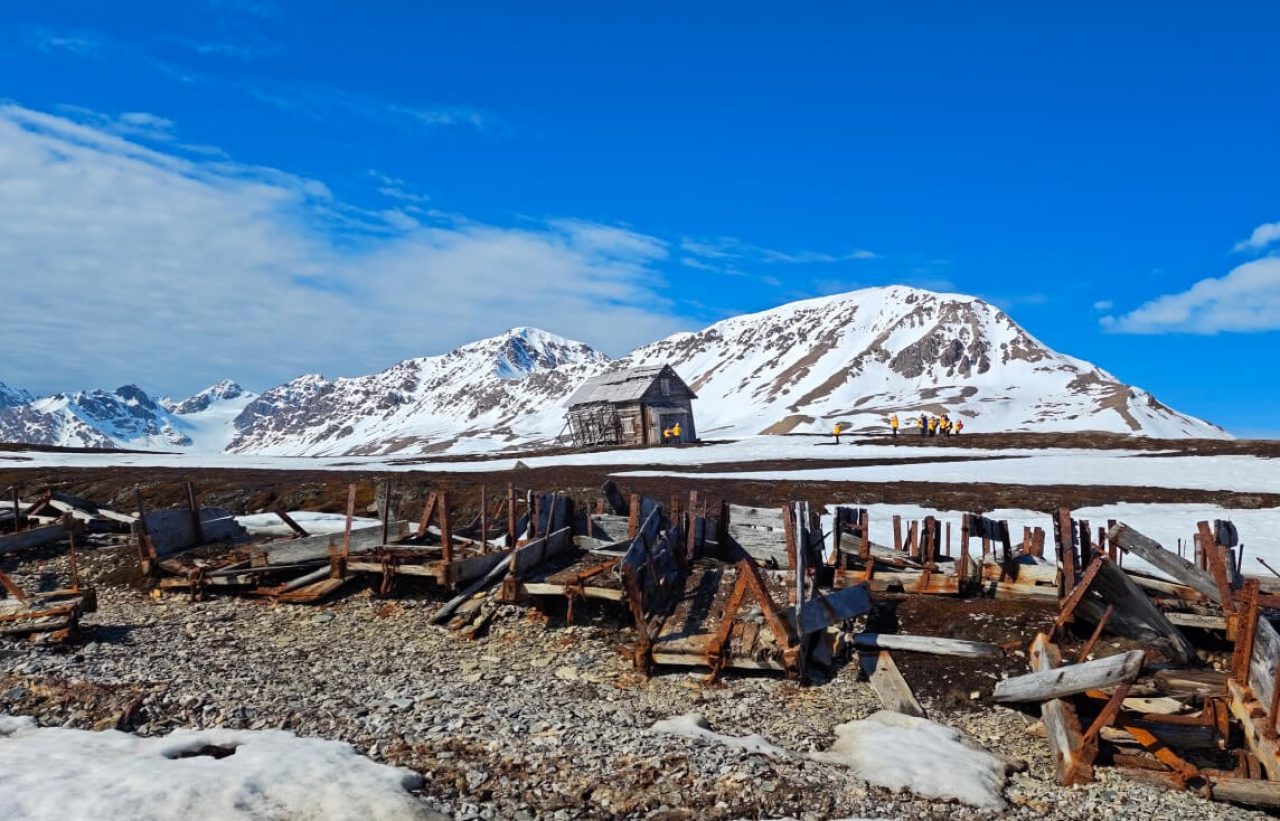 An wooden pier like structure that appears abandoned stretching out over sandy ground. Shot against a deep blue sky.