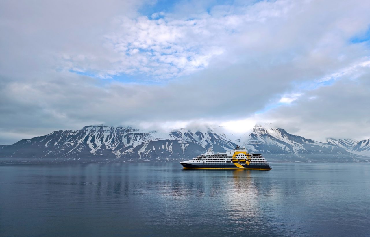 Cruise ship sailing in front of an epic mountain side covered in snow