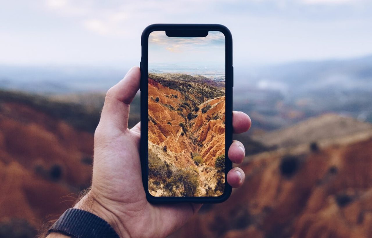 Hand holding a mobile phone in front of a canyon-like landmark