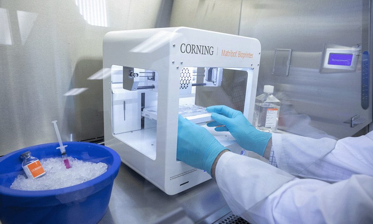 A scientist in a lab with blue-gloved hands works with their hands inside the Matribot printer.