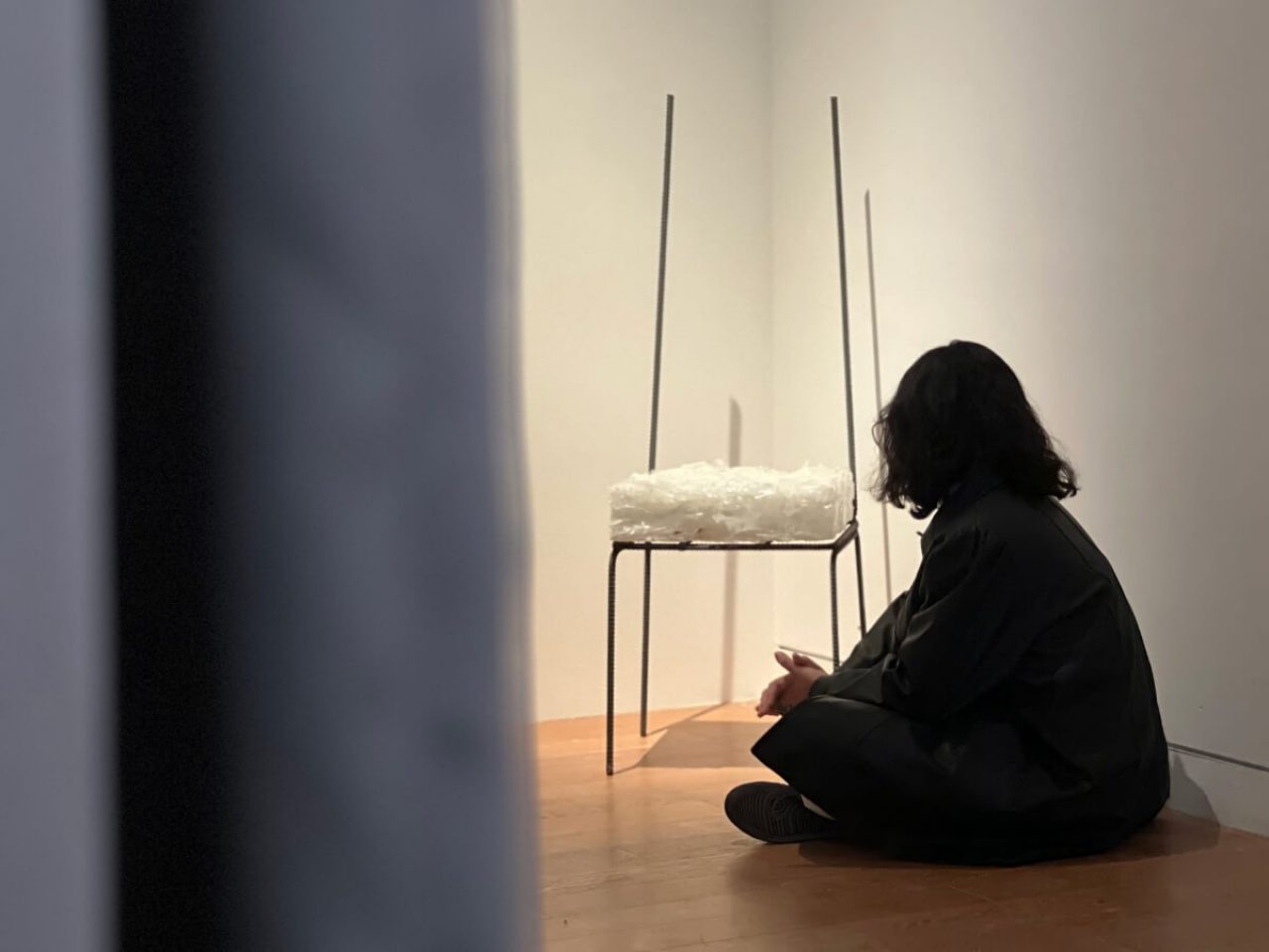 A silhouetted woman sits by the art piece which stands in the corner of a gallery.