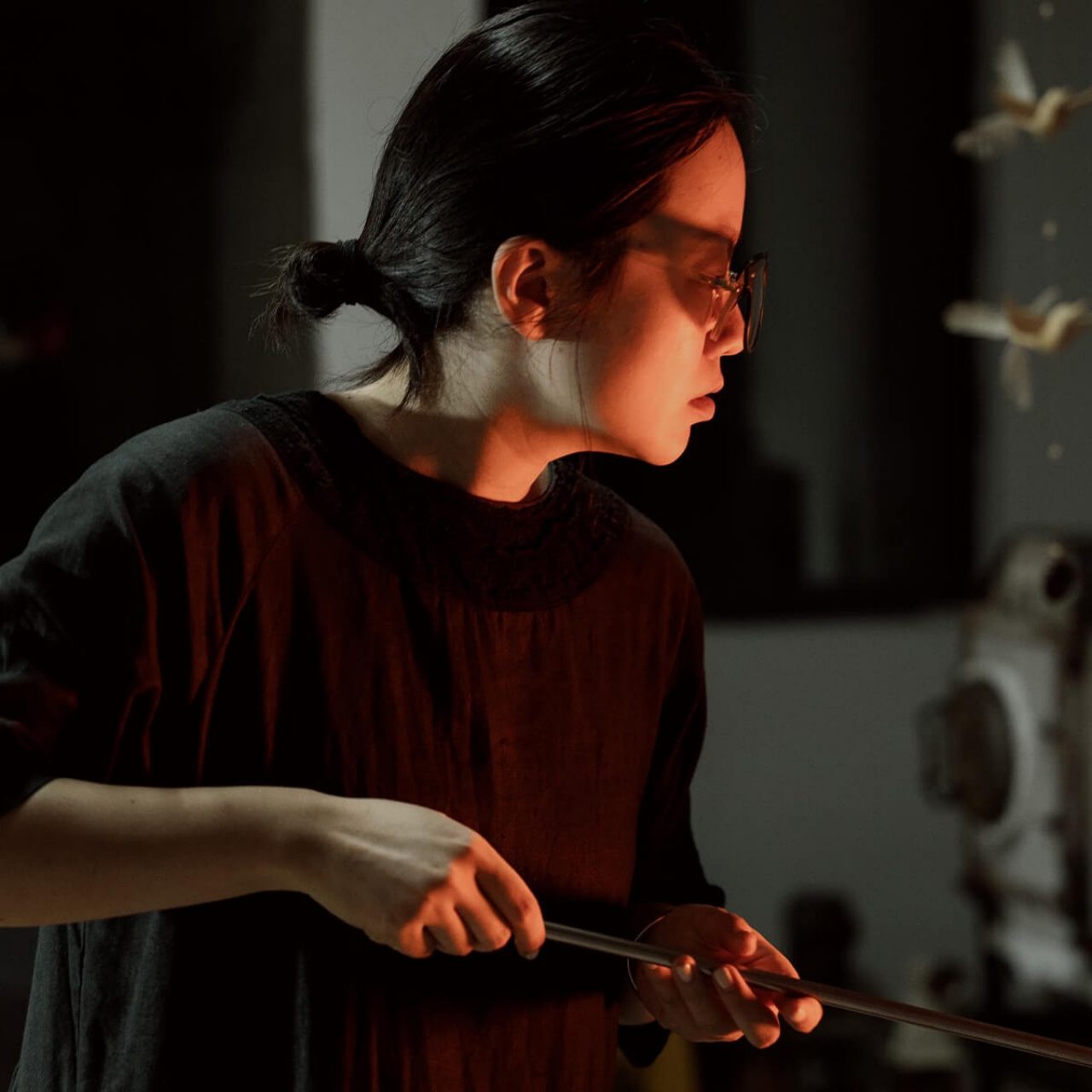 Side profile of Chinyurin wearing dark clothing and glasses working at the furnace