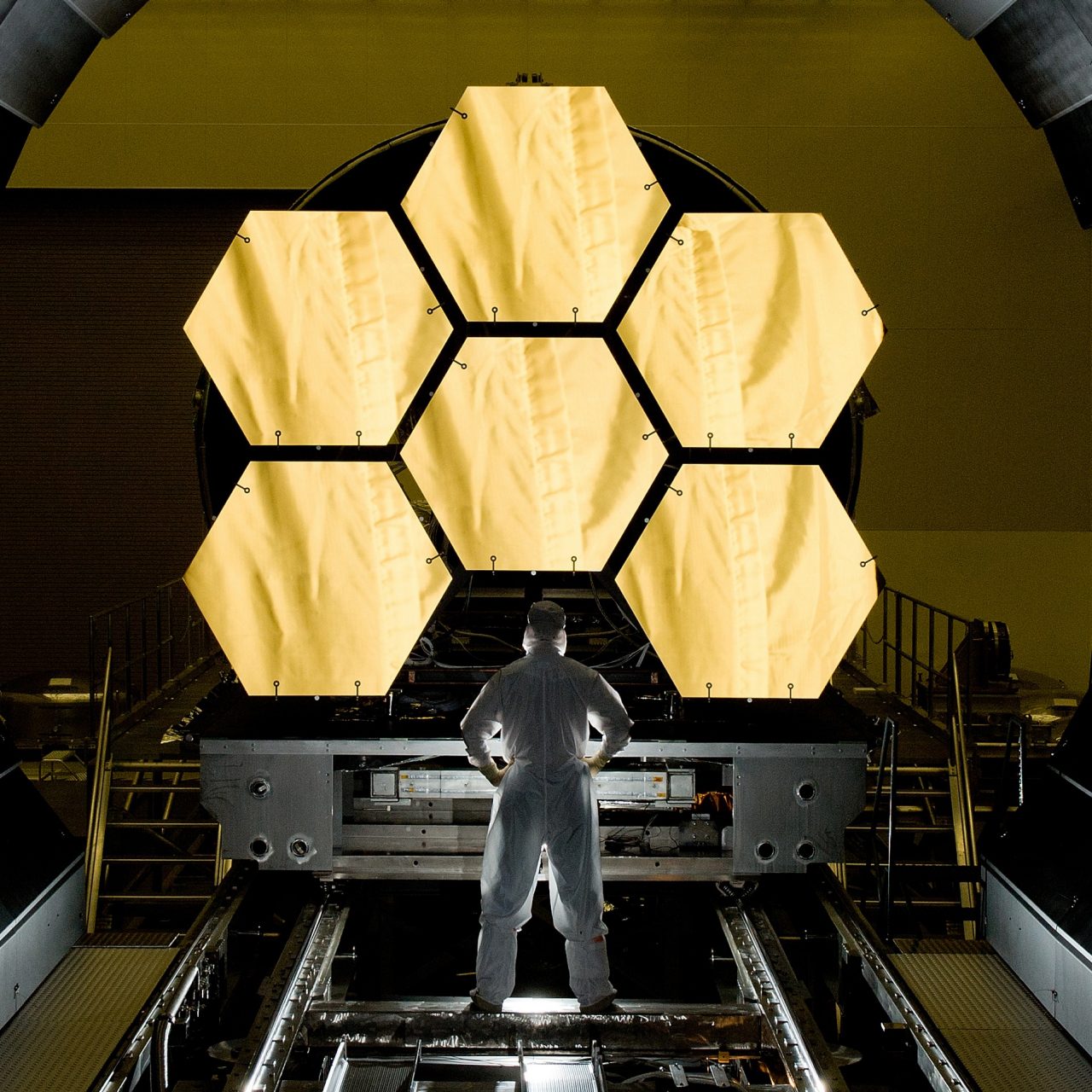 An engineer stands with their back to the camera looking at the James Webb Telescope.