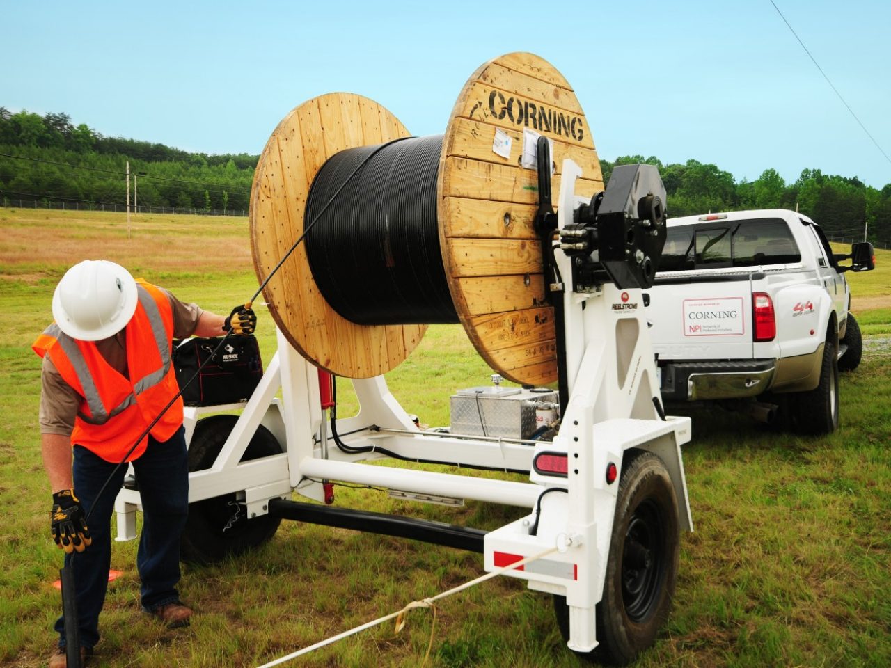 Engineer in high viz vest guiding Corning fiber cable from reel in an open field