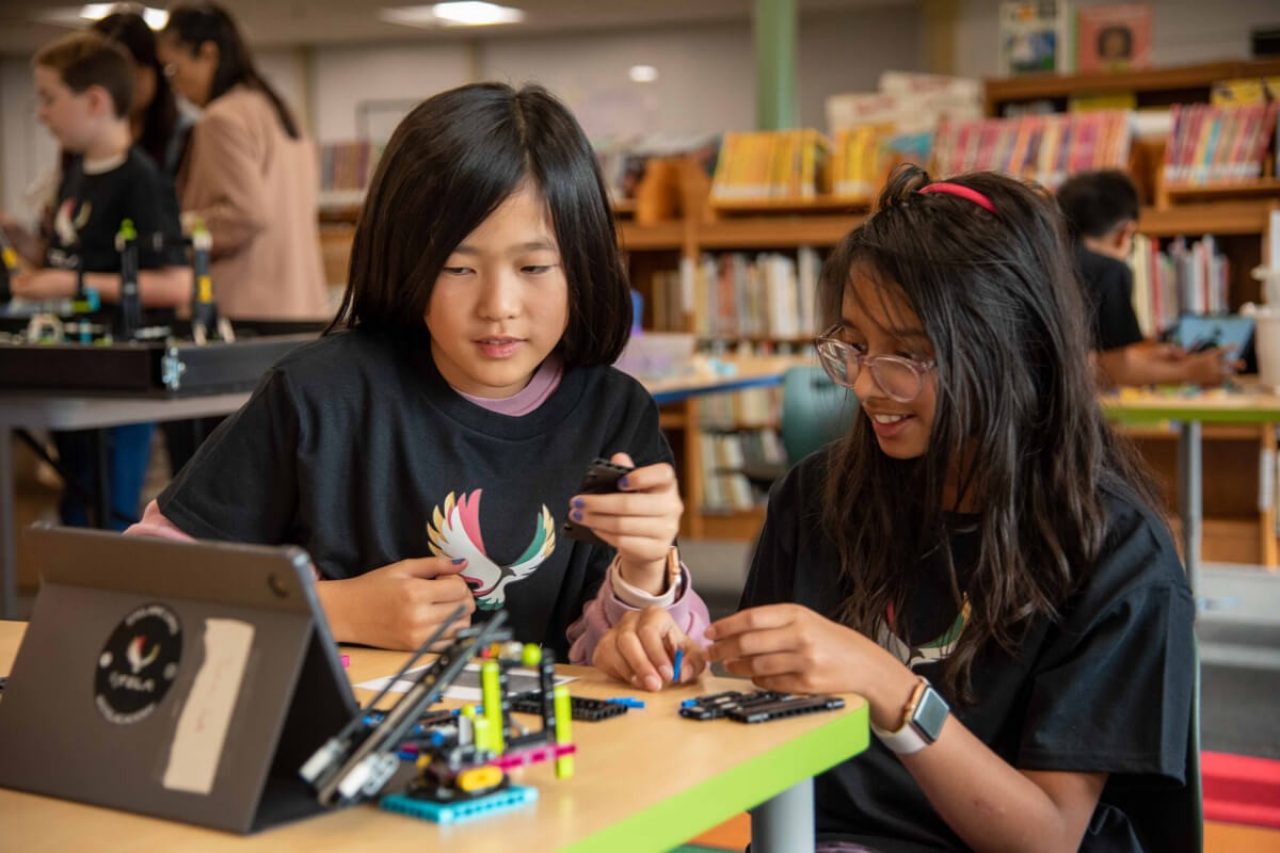 Two STELA students construct a robot while sitting at a table